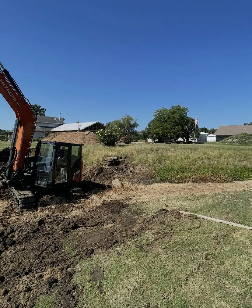 Orange excavator cutting a ditch line along the edge of a yard