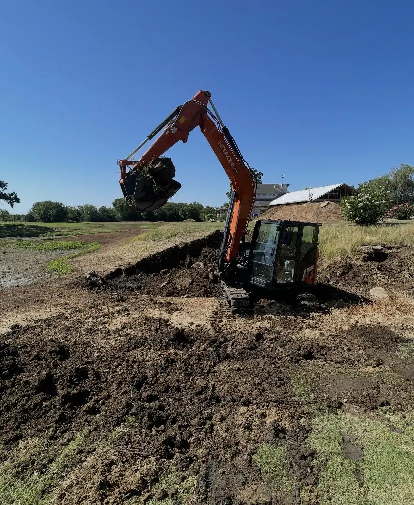 Orange excavator reshaping a bank at the edge of a pasture