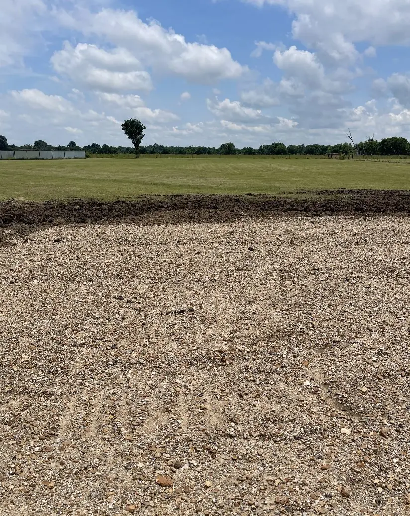 Wide pad of crushed rock graded level at the edge of a field