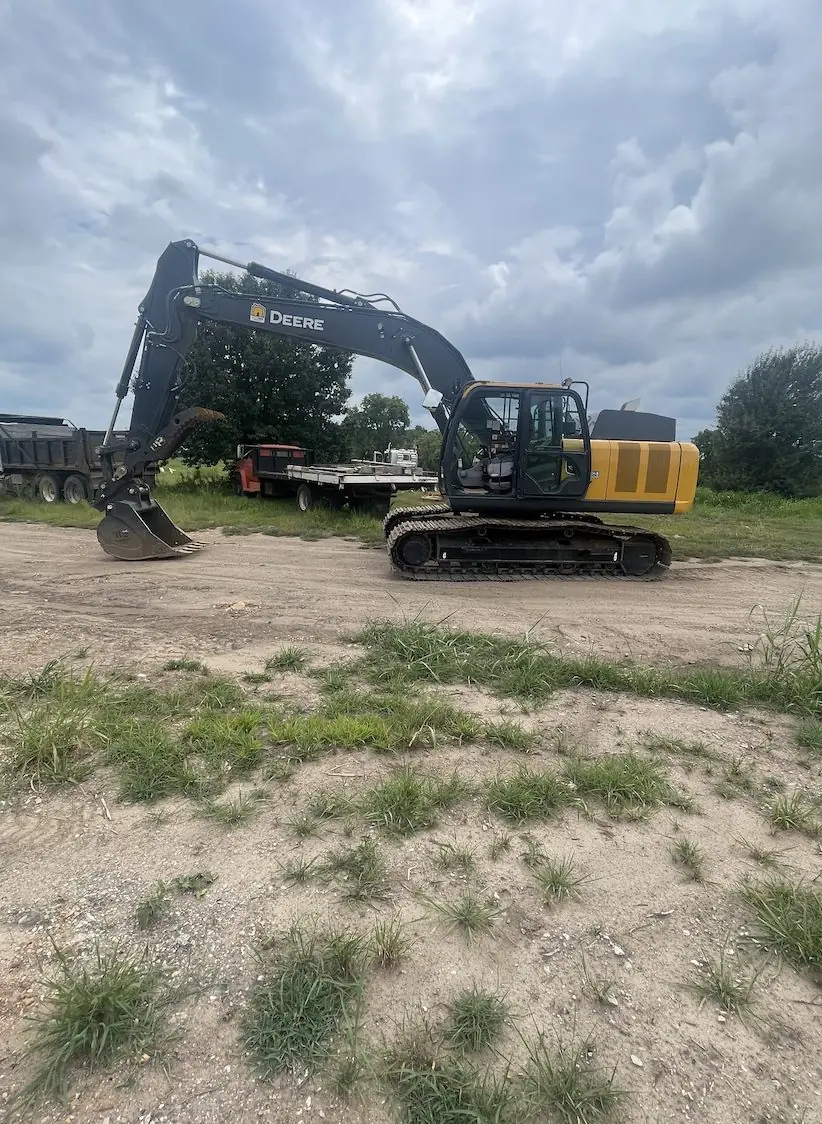 Excavator parked on a dirt yard beside a flatbed trailer