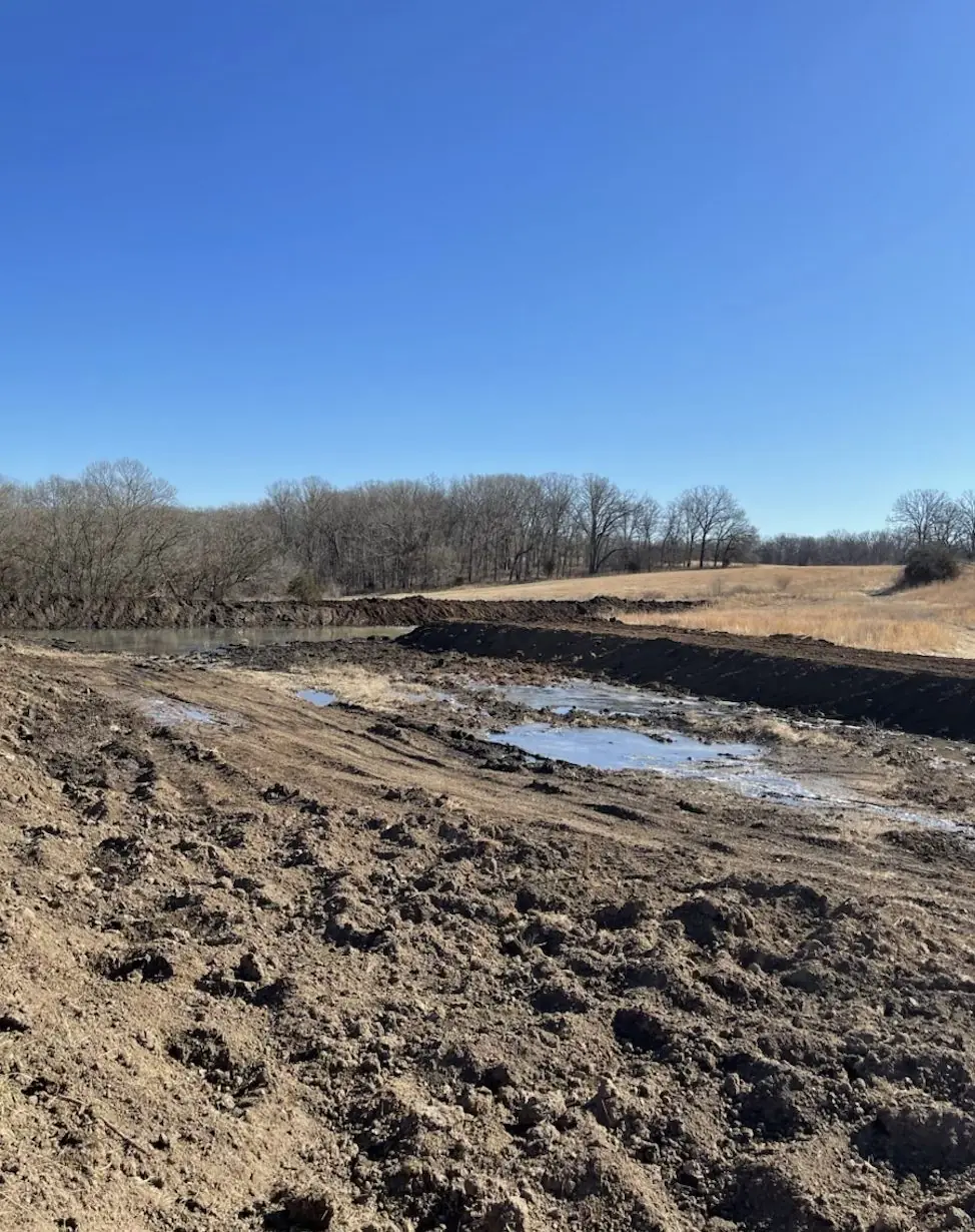 Pond dug out with muddy water in the bottom and a tree line behind